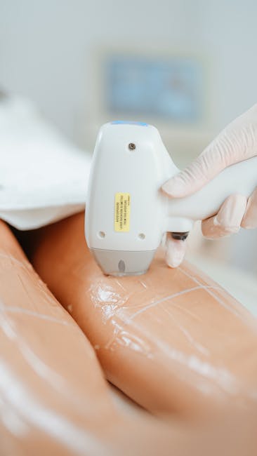 A gloved hand holding a handheld ultrasound or scanning device close to a person's leg, which is covered with a protective transparent film or plastic wrapping. The background shows a blurred medical or clinical setting with a monitor or screen, indicating a professional environment. This image relates to the careful packing and handling involved in house removals, emphasizing proper protection techniques during a home relocation process, as provided by services like Man With a Van Leyton. The scene highlights the importance of secure packing materials and careful handling during furniture and equipment transport within a house move, supporting the topic of packing and moving procedures in house removals and logistics.